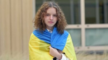 Omuzlarında Ukrayna bayrağı olan liseli bir kızın portresi. Zafere olan inanç. 4K.