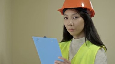 Asian woman builder in protective clothing. A young woman is holding a folder with documents and smiling. HD.