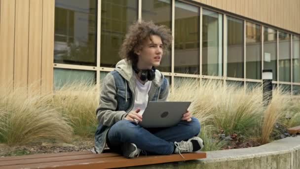 Iemand Met Een Laptop Een Bankje Binnenplaats Van Een Onderwijsinstelling — Stockvideo