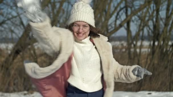 戴着白色针织帽子和眼镜的快乐的少女抛出了一个雪球 — 图库视频影像