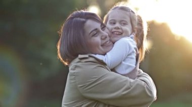 Genç bir kadın yaz parkında gün batımı yürüyüşünde genç kızına nazikçe sarılıyor. 4K.