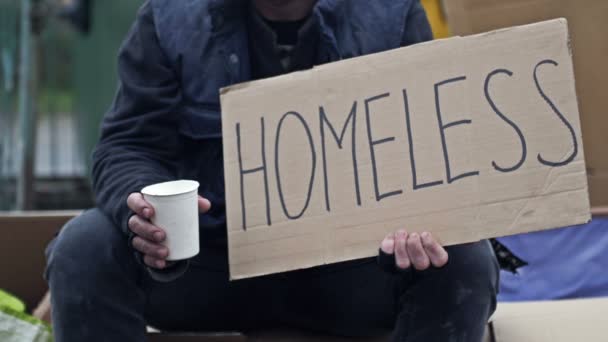Неопрятный Мужчина Сидит Нищим Стаканом Держит Рукописный Плакат Бездомный Сердечные — стоковое видео