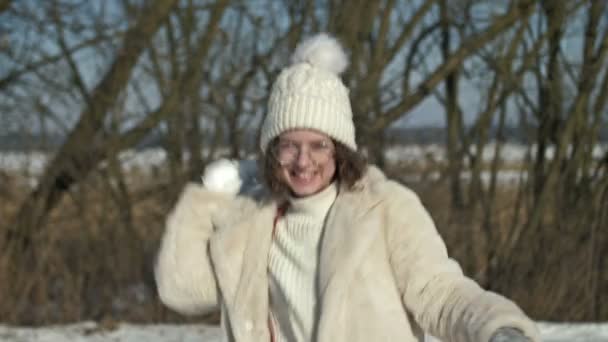 白いニットキャップと眼鏡の陽気な10代の少女は 雪玉を投げます — ストック動画
