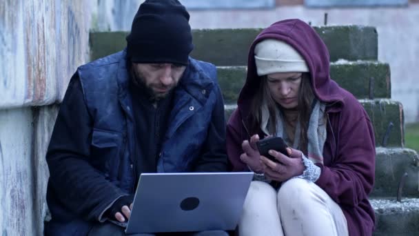两个冻僵的无家可归的人 一个男人 一个女人 坐在街上 他们手里拿着笔记本电脑和手机 这对夫妇正在寻找招聘广告 — 图库视频影像