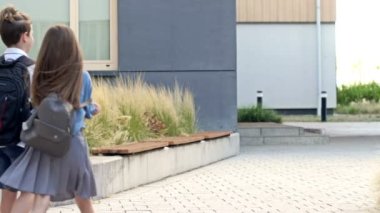 Four elementary school students, two boys and two girls, are walking around the school yard. The children are talking animatedly. Back to school. HD.