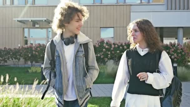 2人のかわいい高校生 男と女の子が教育機関の中庭を歩いています 10代の若者たちが生き生きと話している — ストック動画