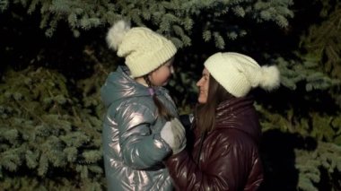 Young woman and her daughter, 7-8 years old, look at each other with love and tenderness. On a walk in the winter forest. 4K.