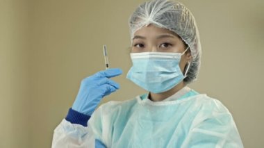 Aşı ve sağlık hizmeti konsepti. Asyalı kadın doktor, tıbbi maske takan hemşire ve aşı şırıngası tutan eldivenler. 4K.
