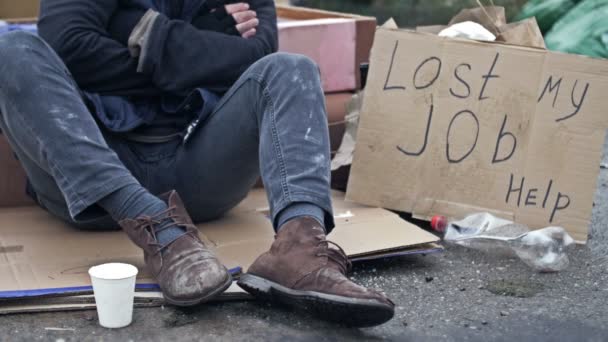在寒冷中颤抖的无家可归的人坐在垃圾堆中的纸板上 在他旁边是一张手写的遗失我的工作帮助海报 — 图库视频影像