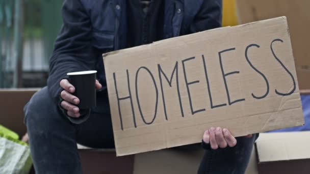 Неопрятный Человек Сидит Чашкой Выпивки Держит Рукописный Плакат Бездомный — стоковое видео