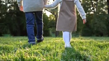 İki küçük çocuk, bir büyük oğlan ve bir küçük kız, parkta el ele tutuşarak yürüyorlar. Gün batımı. Dikiz aynası. HD.