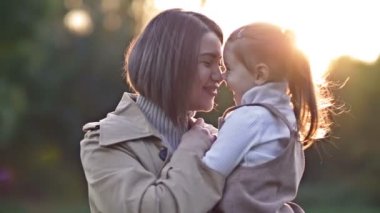 Sevimli, tatlı küçük bir kız bahar parkında yürürken genç annesine sarılıyor. HD.