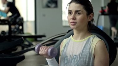 Sıska kız dambılla egzersiz yapıyor. Kollarını sıkan fitness kızı. 4K.