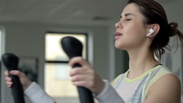 Kulaklıklı Genç Güzel Bir Kadın Spor Salonunda Bir Simülatörle Meşgul — Stok video