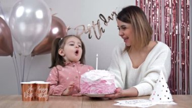 Little girl blows out the candles on her birthday cake, her happy mother is nearby. HD.