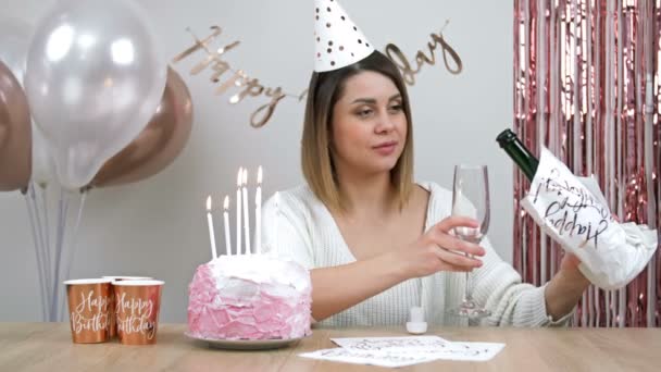 美丽的年轻女子独自庆祝生日 她坐在装饰华丽的墙壁的背景下 在生日蛋糕上吹灭蜡烛 喝香槟 并不伤心 — 图库视频影像