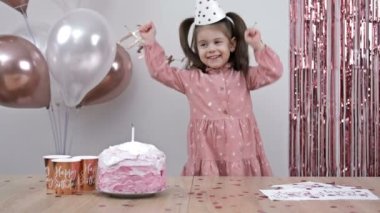 Birthday of a little girl. Child is very happy. Beautifully decorated room, a cake, a shower of glittery confetti. 4K.