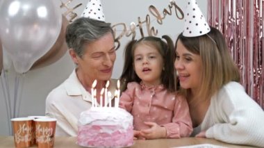 Birthday of a little girl. Next to my mother and grandmother. Child blows out the candles on the birthday cake. HD.