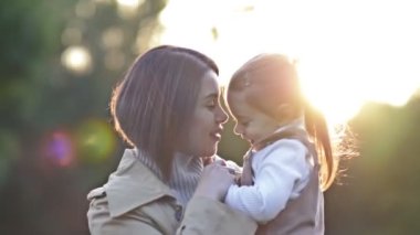 Sevimli, tatlı küçük bir kız bahar parkında yürürken genç annesine sarılıyor. HD.