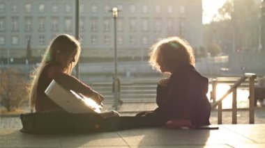 Teenage leisure. Teenage girls sit on the embankment of the city. One is holding a guitar. The girls are having fun. HD.