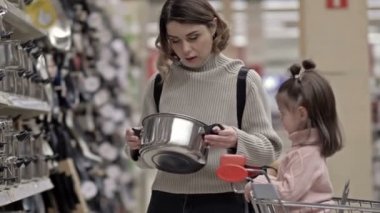 Küçük kızıyla birlikte bir süpermarketin çanak çömlek reyonunda. Bebek arabada oturur ve annesinin seçim yapmasına yardım eder. 4K.