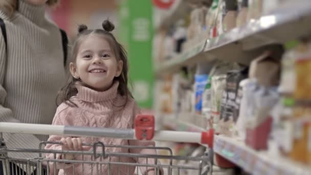 Kleines Mädchen Einem Einkaufswagen Neben Den Regalen Mit Lebensmitteln Einem — Stockvideo