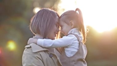 Sevimli, tatlı küçük bir kız bahar parkında yürürken genç annesine sarılıyor. HD.