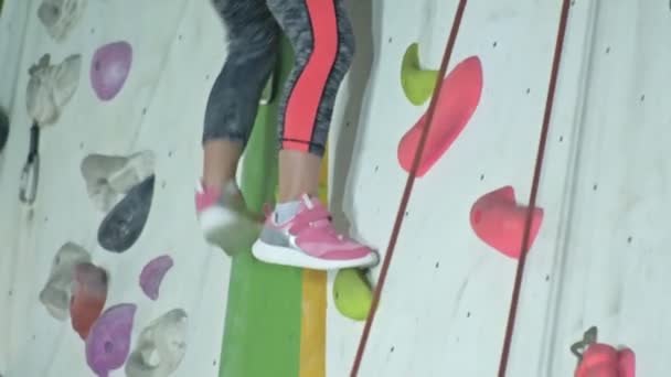 ピンクのスニーカーで女の子の足は ホールドにもたれて 登山壁を下り坂 — ストック動画