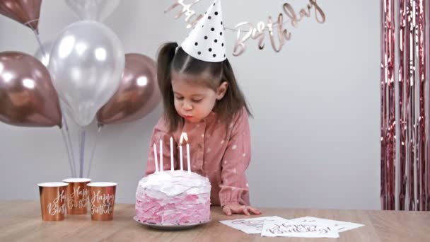 かわいい女の子は風船を背景に自宅で誕生日ケーキの上にろうそくを吹き消します 子供の誕生日だ — ストック動画