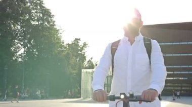 Elektrikli scooterlı güneş gözlüklü bir adam şehir meydanında geziyor. Uygun ve çevre dostu bireysel şehir taşımacılığı kavramı. 4K.
