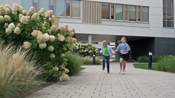 两名8 9岁的男孩和女孩手牵着手在学校院子里跑来跑去 学校的友谊4K — 图库视频影像