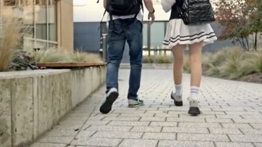 İki lise öğrencisi, bir erkek ve bir kız, sınıfa gidin. Gençler hareketli konuşuyorlar. Arkadan bak. HD.
