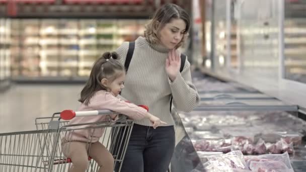 슈퍼마켓에서 고기를 진열장 근처에 아이들은 식료품 카트에 앉아서 엄마가 선택하도록 — 비디오