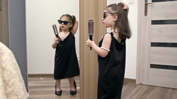 穿着妈妈鞋子 戴着太阳镜 手里拿着梳子的淘气小女孩在镜子前模仿歌手 — 图库视频影像
