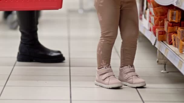スーパーの棚の近くに赤い食料品のバスケットを持つ女性の子供の足と足 — ストック動画