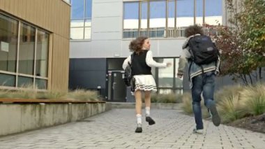 İki öğrenci, bir kız ve bir erkek, eğitim enstitüsünün avlusunda koşuşturuyorlar. Sınıf arkadaşlarının acelesi var. Derse geç kaldım. 4K.