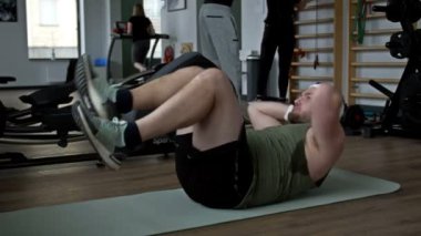 Şişman adam spor salonunda paspasın üzerinde yatarken özenle egzersiz yapıyor. HD.