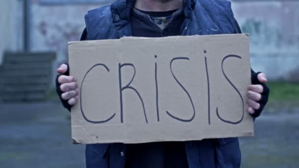 一个不整洁的男人坐在街上 手里拿着一张手写的Crisis海报 — 图库视频影像