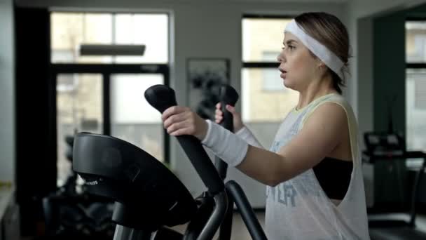 强壮的年轻漂亮的女人在椭球上的体育馆里锻炼 体育和健康生活方式的概念 — 图库视频影像