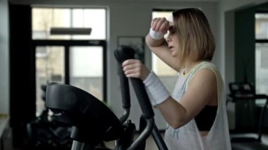 Genç ve güçlü bir kadın spor salonundaki simülatörle meşgul. Kadın yorgun. Spor ve sağlıklı yaşam tarzı kavramı. 4K.