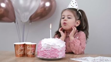 Küçük kız evdeki bir doğum günü pastasının üzerine mum üflüyor. Childs 'ın doğum günü. HD.