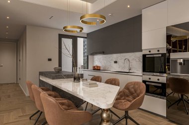 Geniş, modern mutfak, beyaz ada ve yemek masasının yanında paslanmaz çelik aletler.