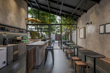 Samimi bir kahveci, ahşap tabure, kahve makinesi, hamur işleri ve kolye ışıkları.