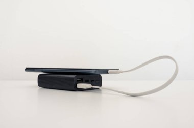 Masadaki siyah güç bankasından şarj olan cep telefonu. Beyaz arkaplan.