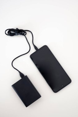 Siyah enerji bankası siyah cep telefonunu şarj ediyor. Modelleme. Siyah kablo. İkisi de beyaz arka planda..