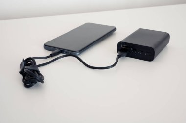 Siyah enerji bankası cep telefonunu şarj ediyor. Siyah kablo. İkisi de beyaz arka planda..