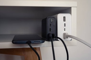 Siyah güç bankasıyla çalışan akıllı telefon. Yanında beyaz güç bankası var. Hepsi beyaz masada.