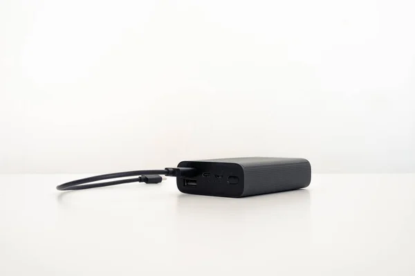 桌上有一个带黑色连接电缆的黑色移动式充电器 通常为白色背景 — 图库照片