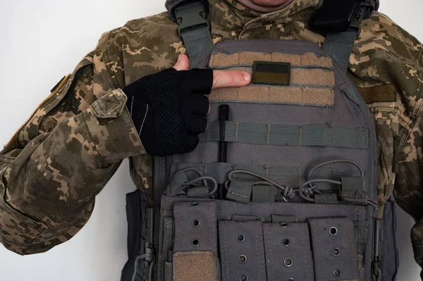 Ukrainian soldier in military pixel unform and bulletproof vest jacket with banner of flag of Ukraine and finger in black glove.