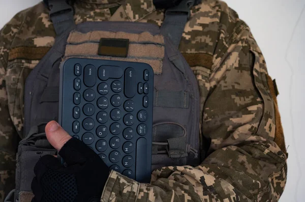 Ukrainian soldier in grey bulletproof jacket with icon of ukrainian flag and keyboard in arm in black glove.